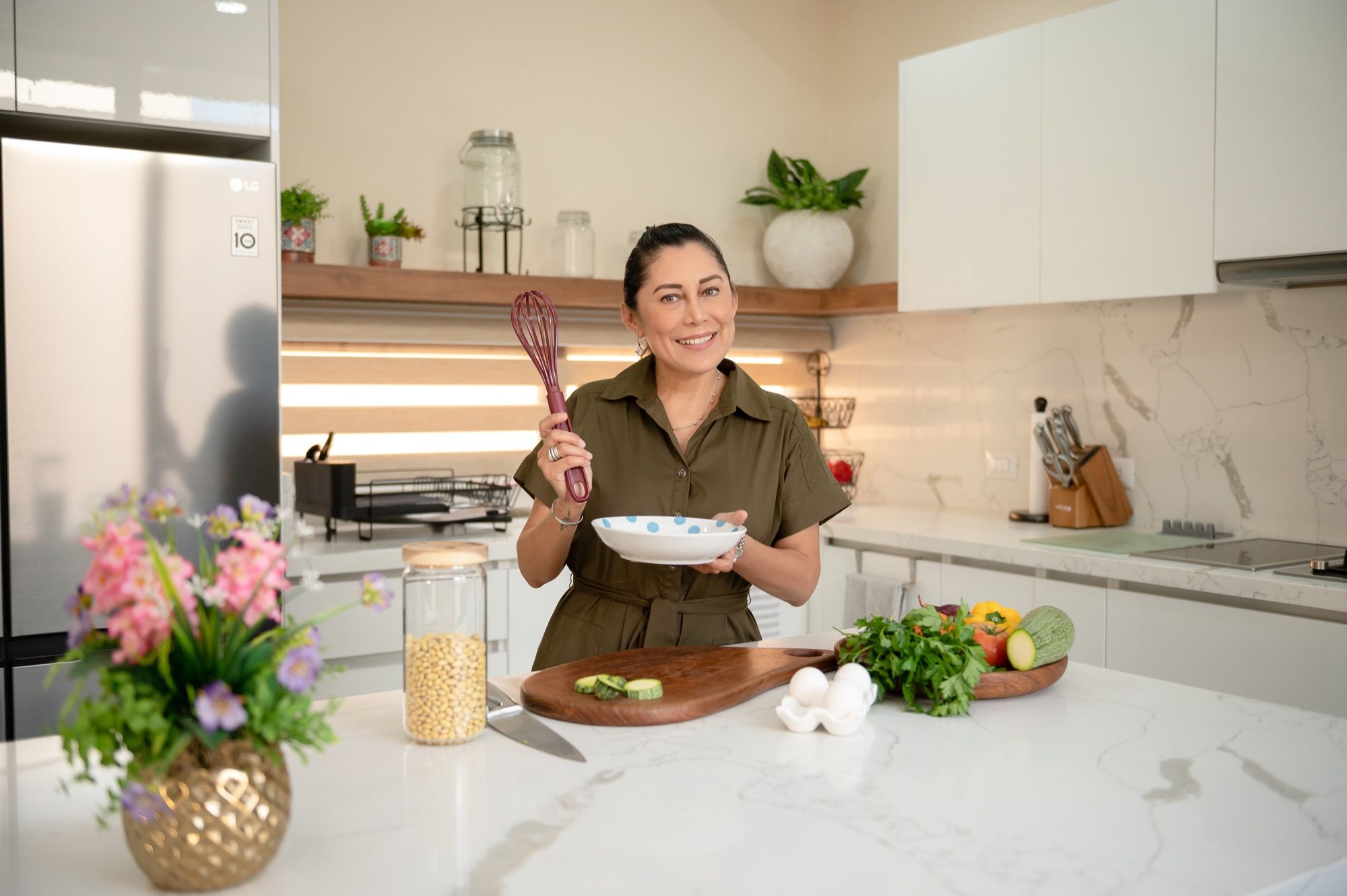 Addy sonriendo con un batidor y un plato en su cocina